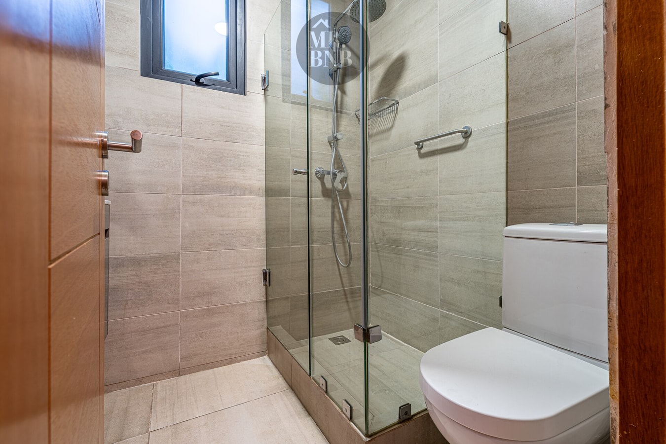 Baño con ducha de vidrio, WC y puerta de madera