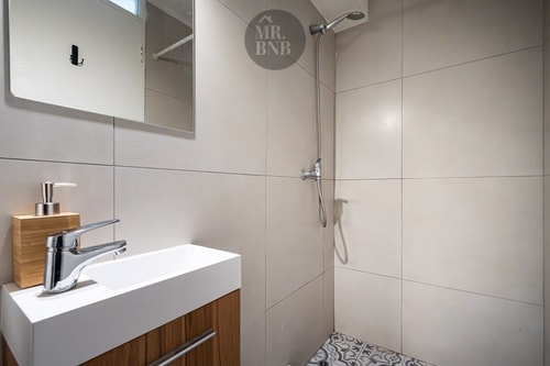 Baño con ducha de vidrio, lavamanos sobre mueble de madera y piso decorado