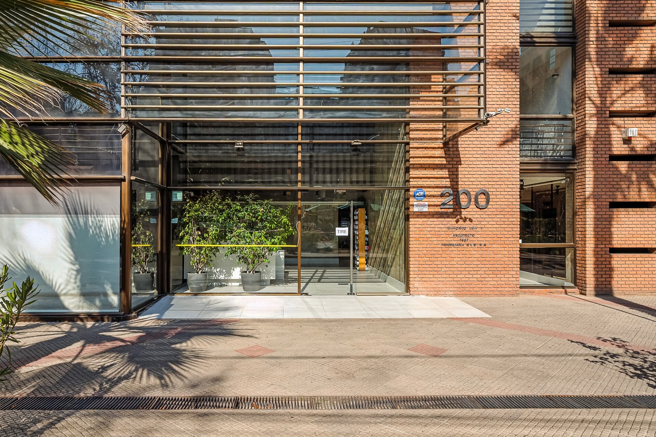 Acceso y fachada del edificio con hall vidriado y vegetación