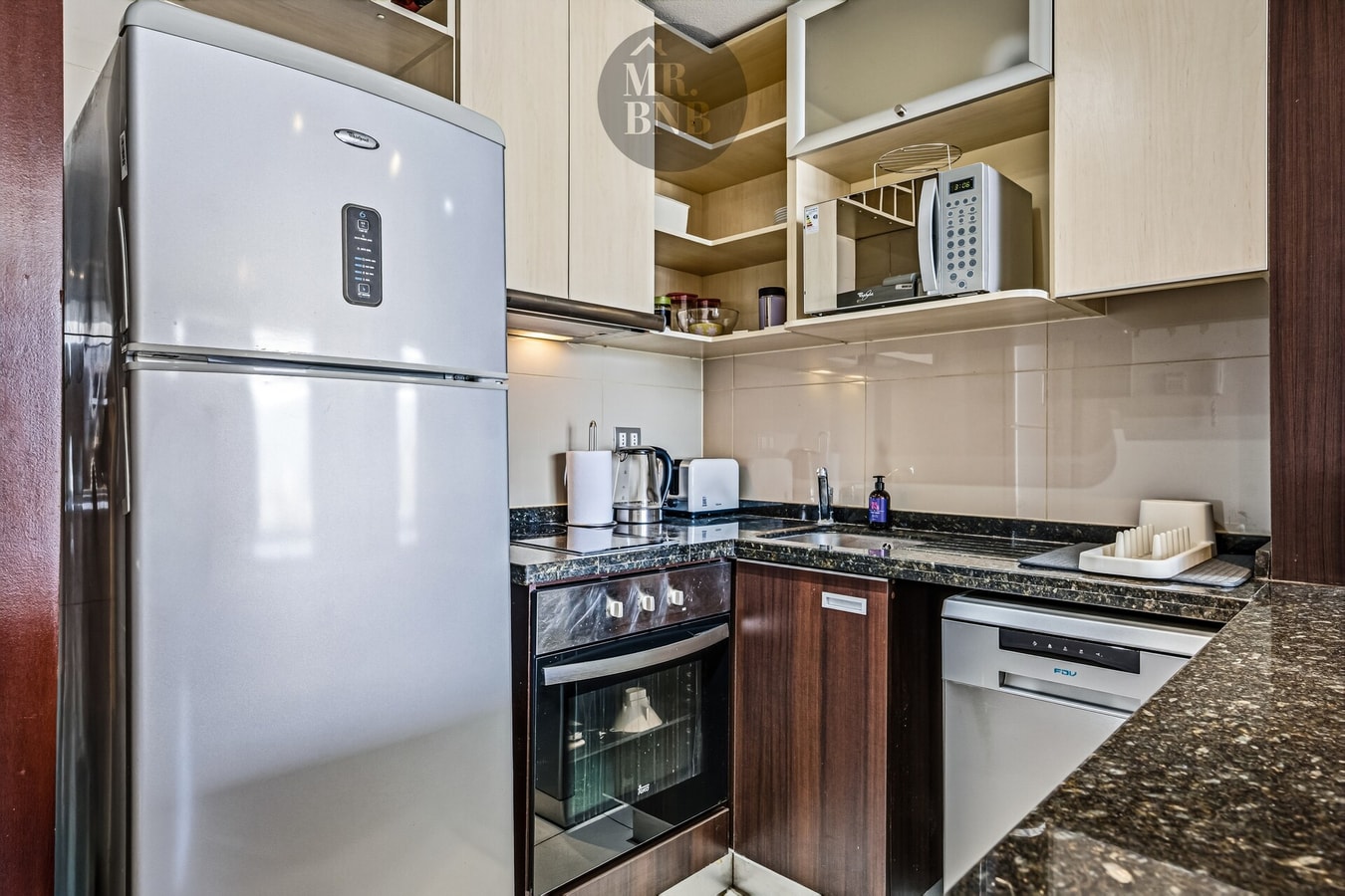 Cocina con refrigerador, horno, lavaplatos y muebles en tonos oscuros