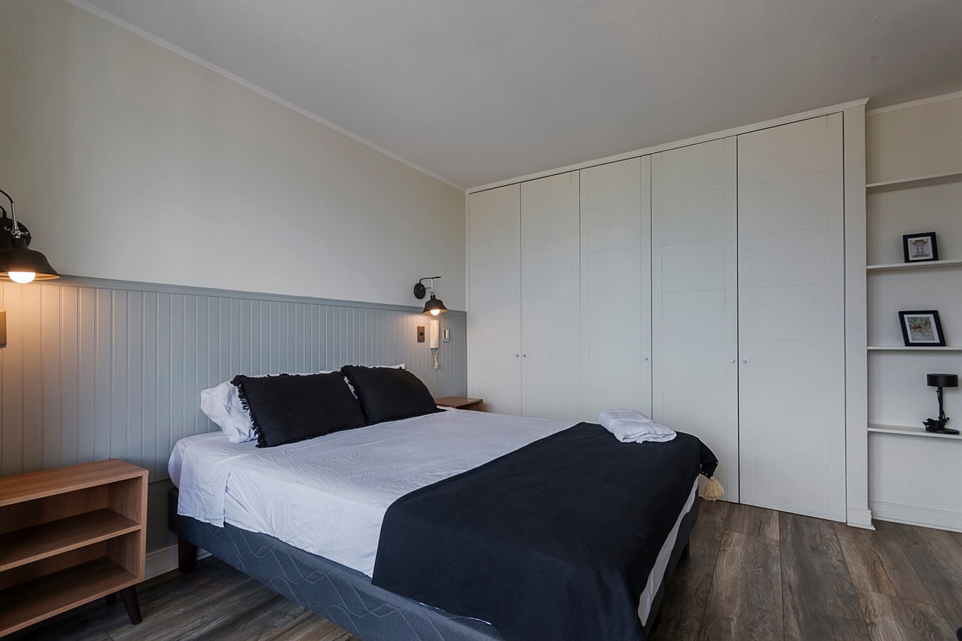 Dormitorio con cama, veladores, closet blanco y repisas con cuadros