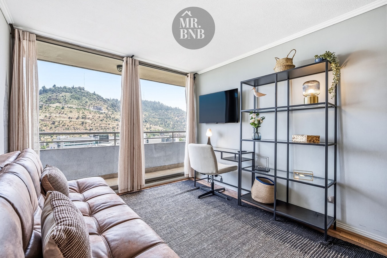 Living con sofá, repisas metálicas y ventanal con vista al cerro.