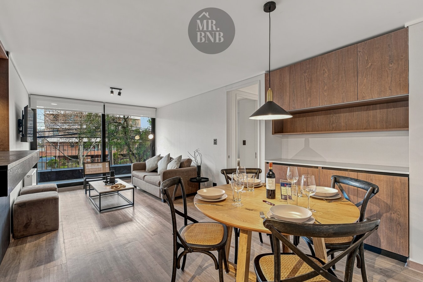 Living comedor con mesa redonda de madera, sillas oscuras y copas dispuestas