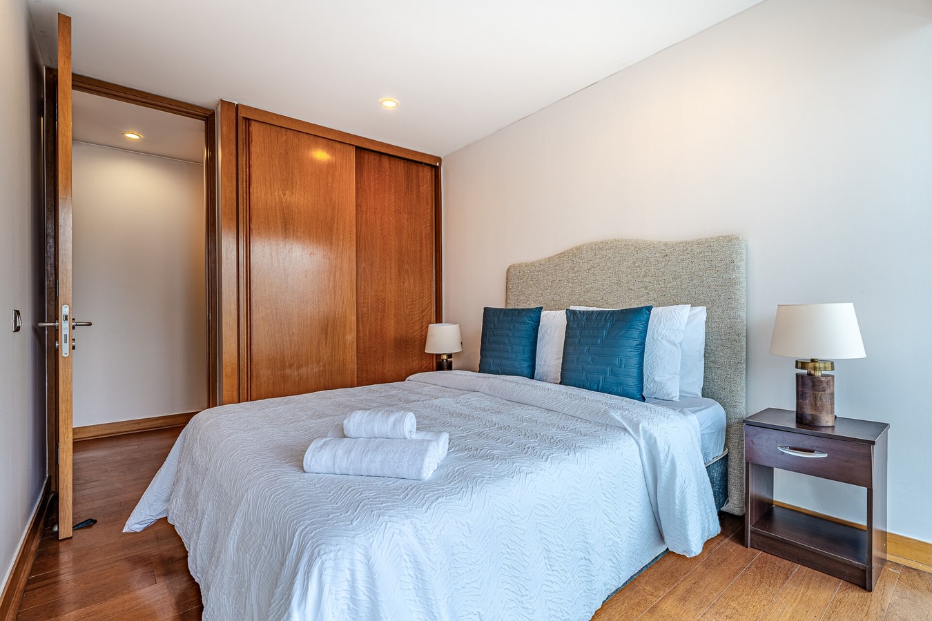 Dormitorio con cama, closet de madera y veladores con lámparas.