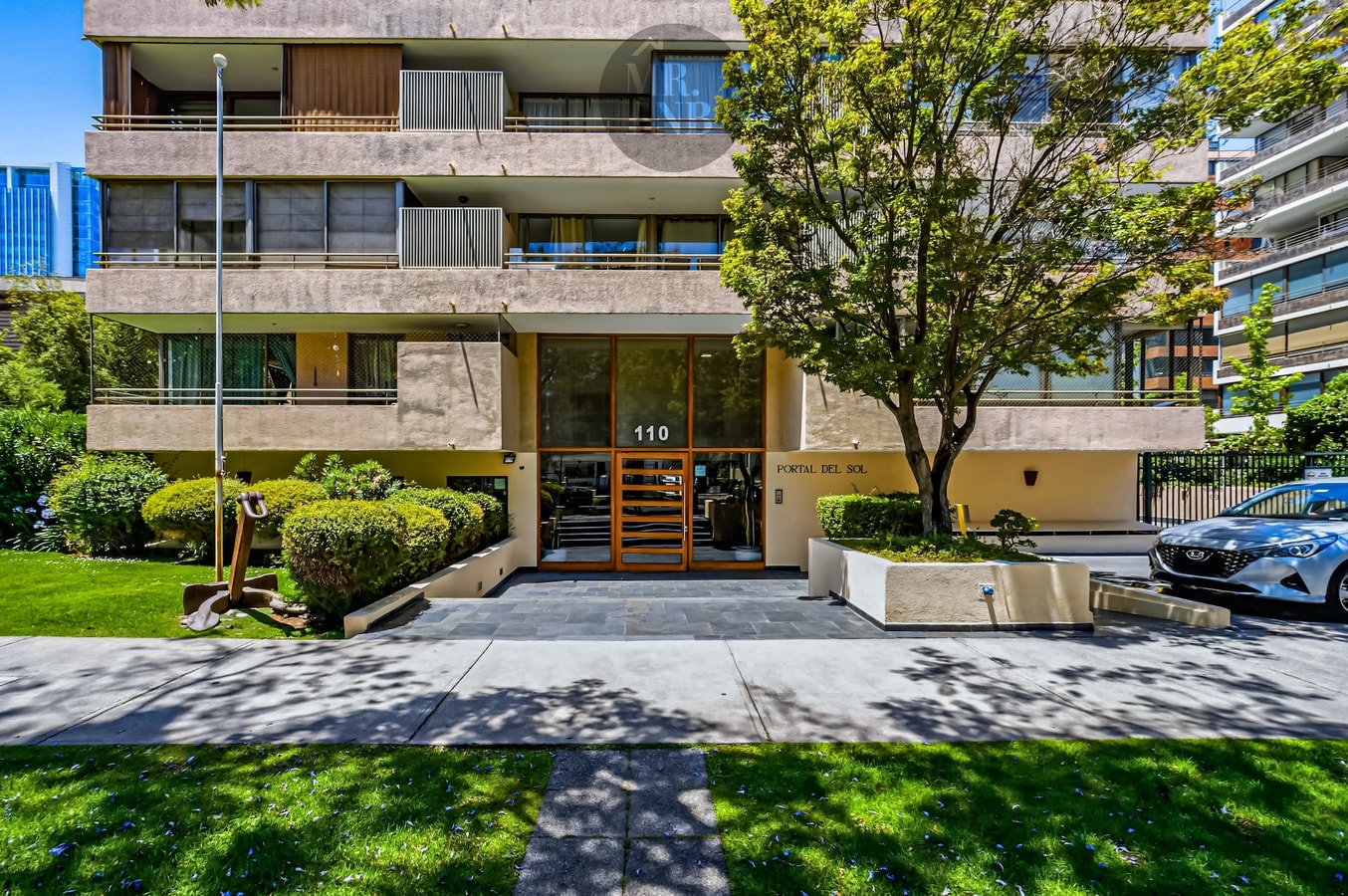 Fachada del edificio con jardín, arbolado y acceso principal.