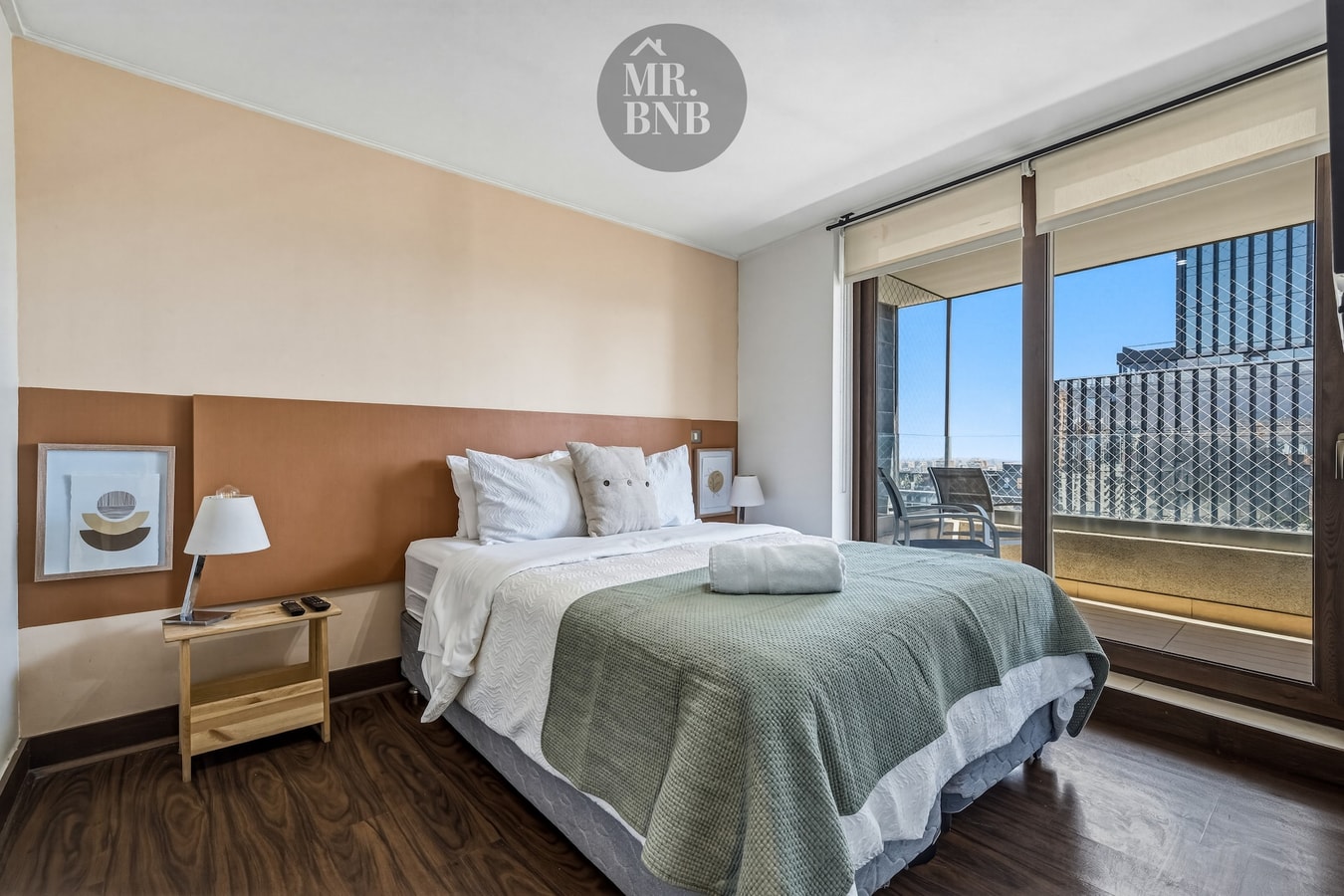 Dormitorio con cama queen, cabecera tapizada, velador con lámpara y ventana.