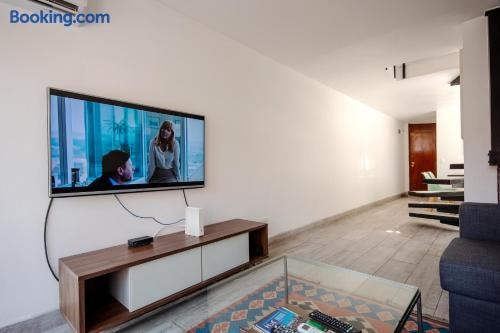 Living con sofá gris, mueble de televisor con pantalla y piso de madera, pasillo hacia escalera al fondo