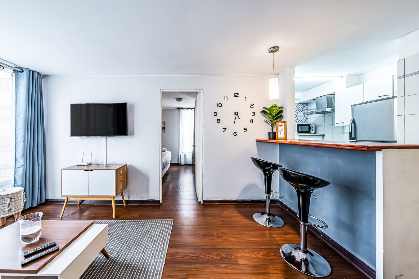Living con barra de cocina, banquetas negras, televisor y reloj de pared