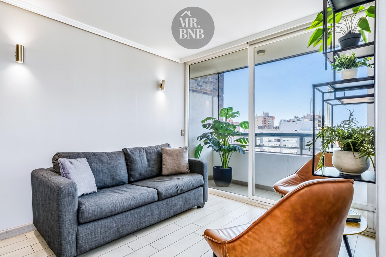 Living con sofá, sillón de cuero, repisas con plantas y ventanal hacia terraza