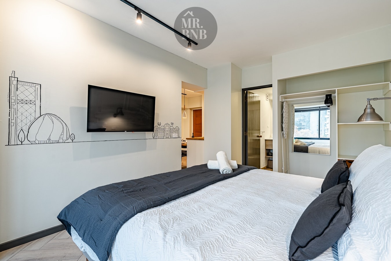 Dormitorio con cama, TV en la pared, mural con dibujo y puerta al fondo