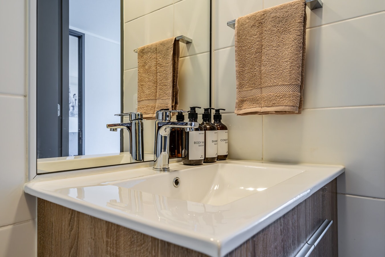 Detalle de lavamanos con toallas y amenities en frascos sobre mesón de mueble oscuro.