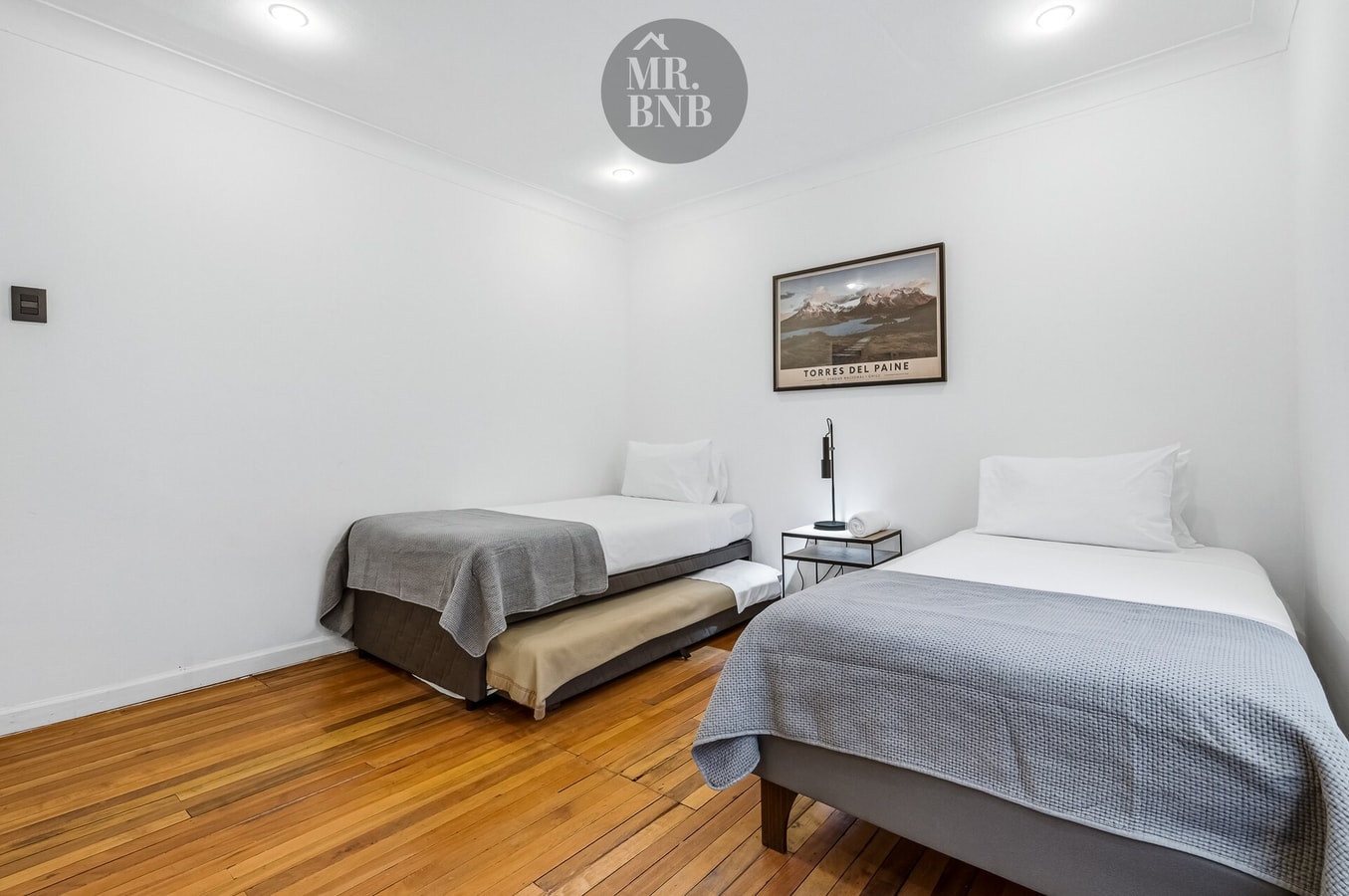 Dormitorio con dos camas individuales, una con cama nido, y veladores entre ambas.