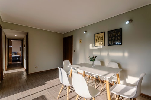 Comedor con mesa blanca y sillas junto al pasillo hacia los dormitorios.