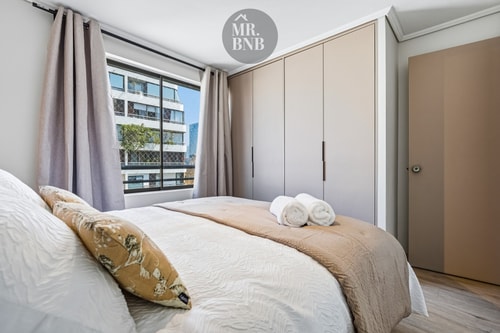 Dormitorio con cama, closets empotrados y ventana amplia con vista a edificios