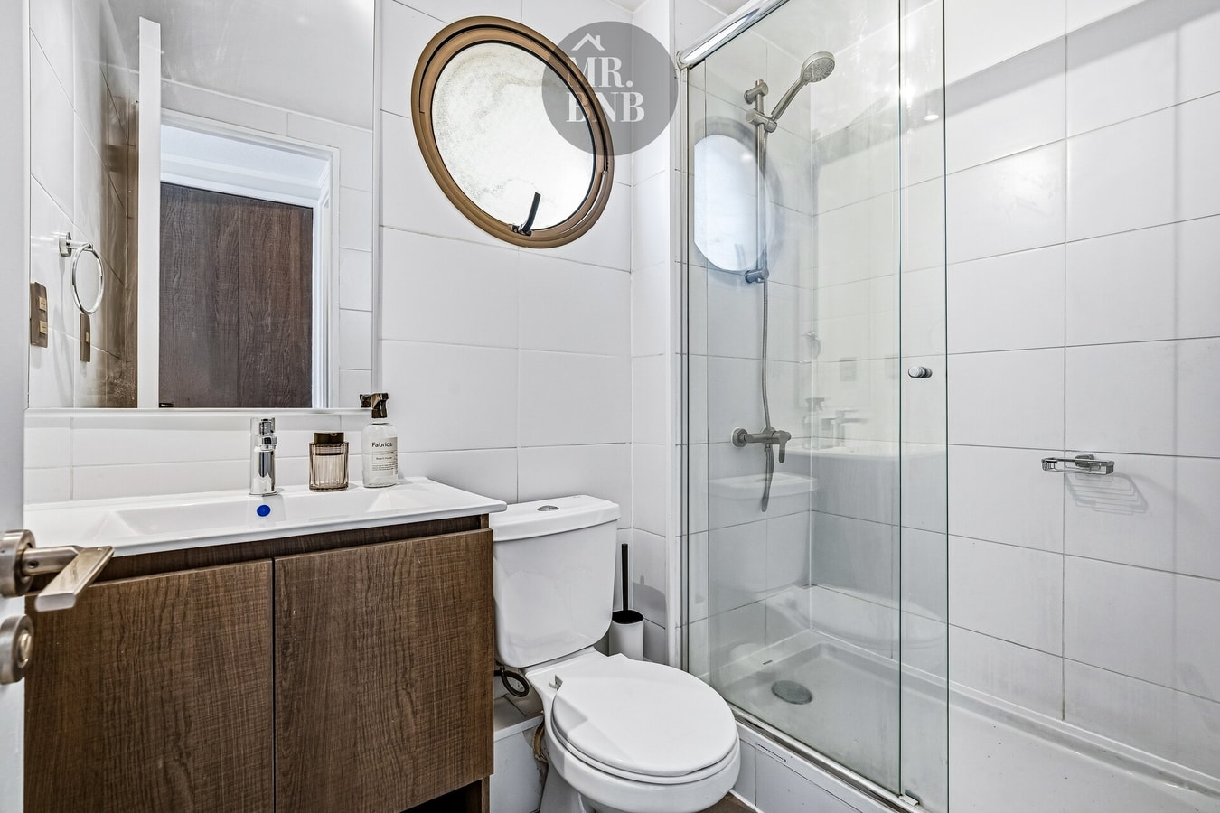 Baño con mueble de madera oscura, lavamanos, inodoro y ducha de vidrio