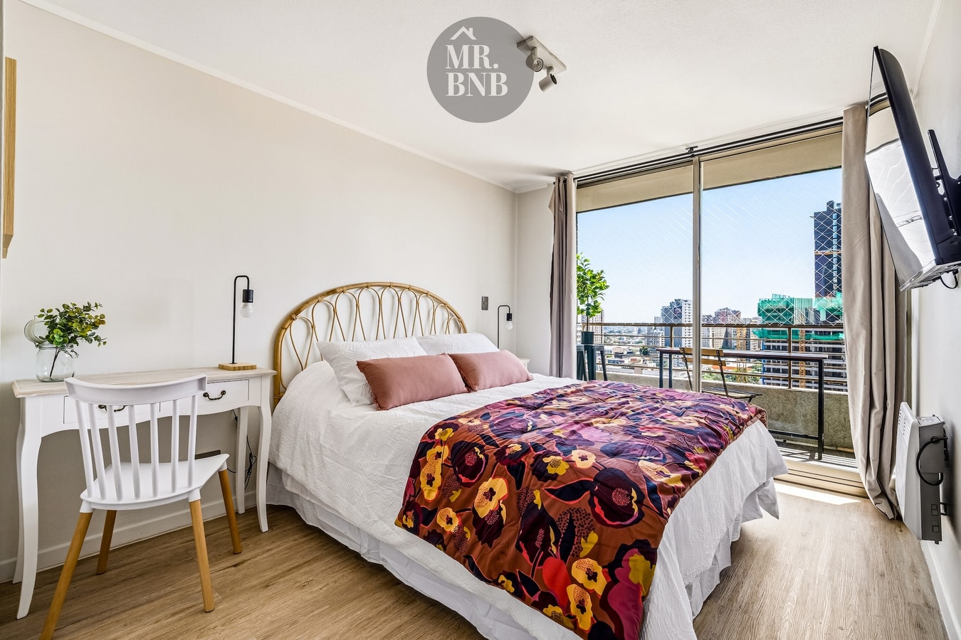 Dormitorio con cama, escritorio, silla y ventanal con vista a la ciudad