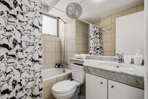 Baño con cortina estampada, tina, inodoro y lavamanos de mármol.