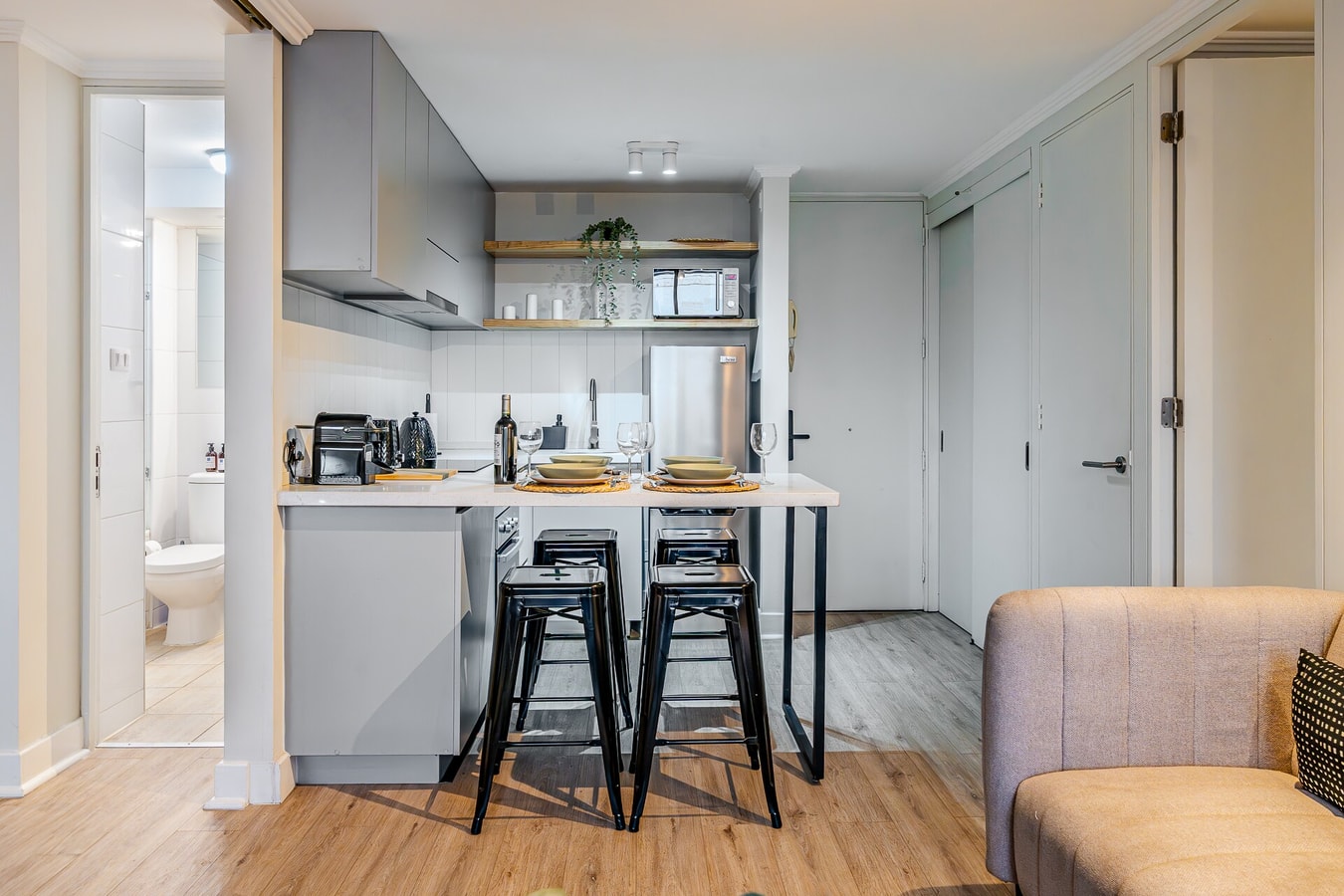 Cocina con barra y banquetas negras, living con sofá claro al fondo