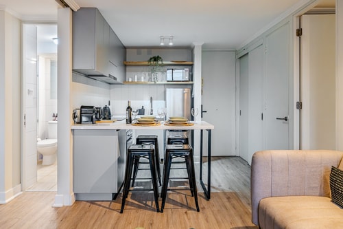Cocina con barra y banquetas negras, living con sofá claro al fondo