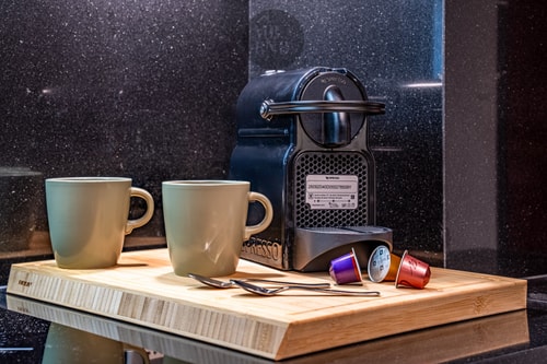 Detalle de cafetera de cápsulas con dos tazas sobre tabla de madera, fondo oscuro