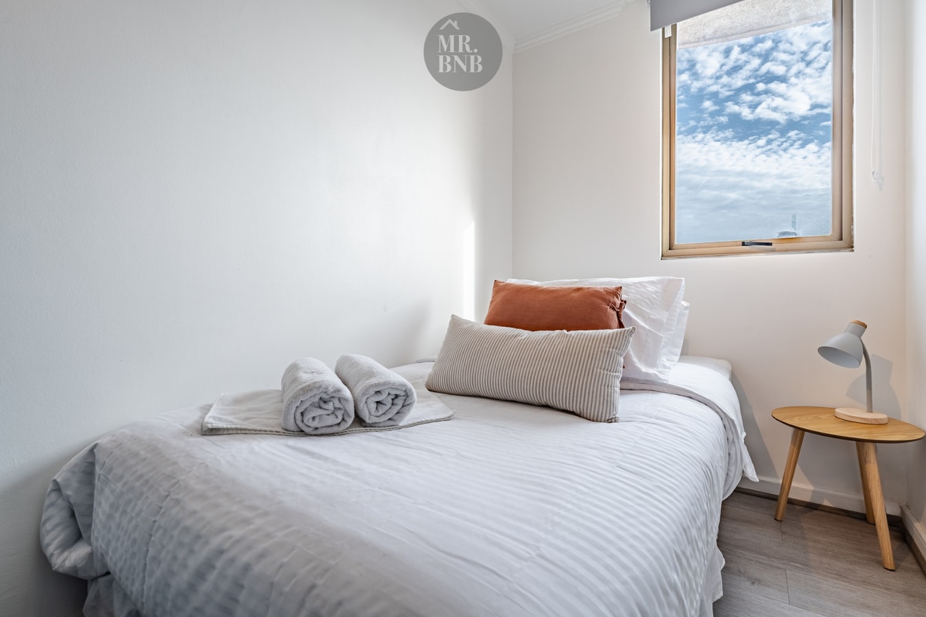 Dormitorio con cama individual, velador de madera y ventana lateral con luz natural