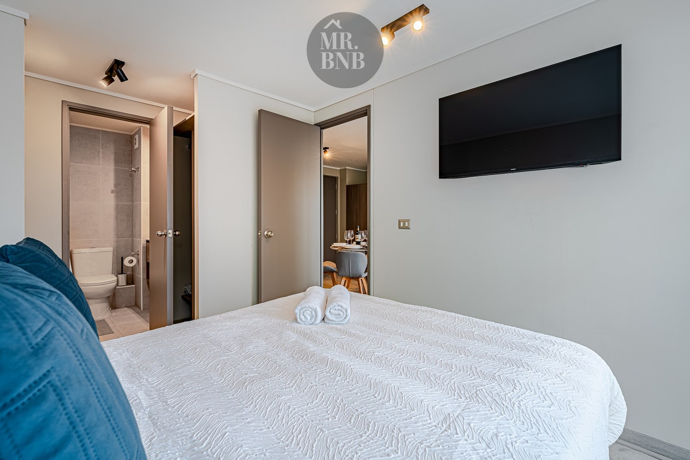 Dormitorio con cama de dos plazas, TV de pared y puerta hacia el baño.