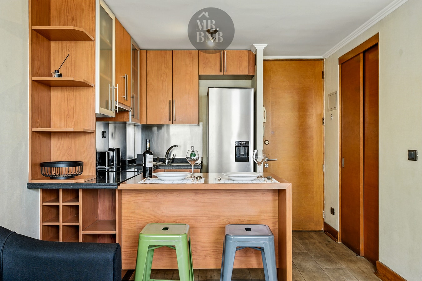 Cocina con isla, taburetes de colores, refrigerador y muebles de madera