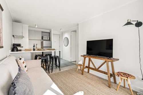Living con sofá, mesa auxiliar de madera, televisor y cocina al fondo