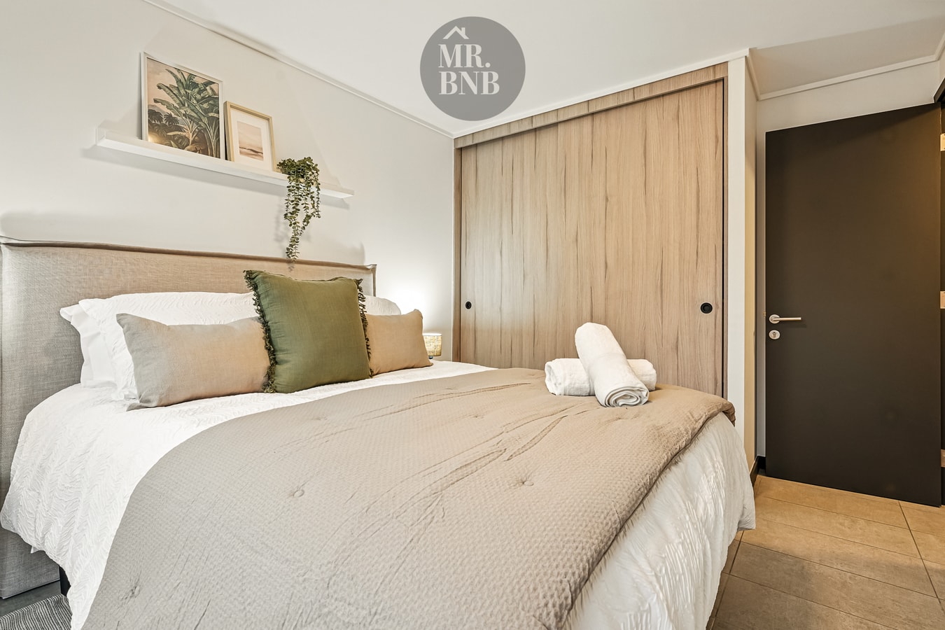 Dormitorio con cabecera tapizada, cojines, toallas y puertas de closet de madera