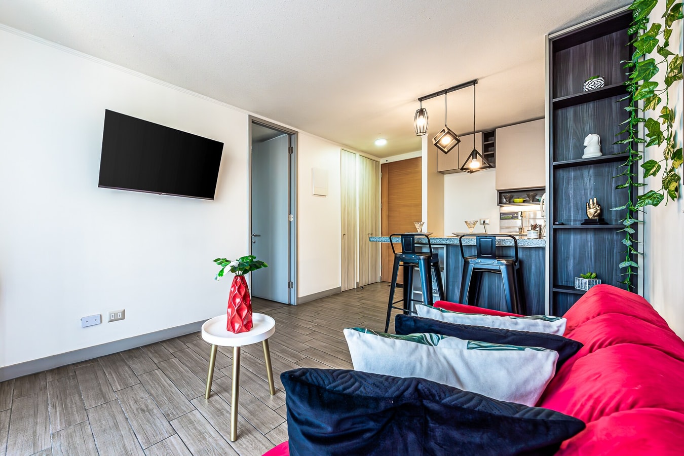 Living con sofá cama azul y rojo, televisor montado en la pared y repisas decorativas