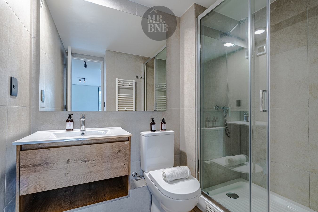 Baño con mueble de madera, doble lavamanos, espejo, inodoro y ducha de vidrio
