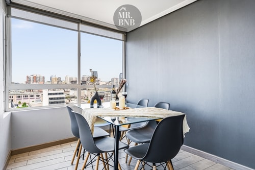 Comedor con mesa de vidrio, sillas negras y ventanal con vista a la ciudad