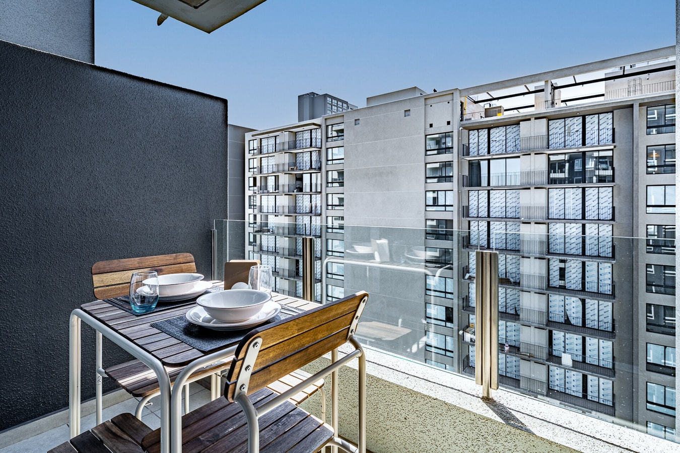 Terraza propia con mesa y dos sillas de madera, mampara divisoria y vista a los edificios vecinos.