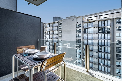 Terraza propia con mesa y dos sillas de madera, mampara divisoria y vista a los edificios vecinos.