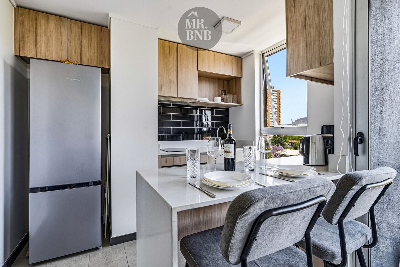 Cocina con refrigerador, barra alta con sillas y vista despejada desde la ventana