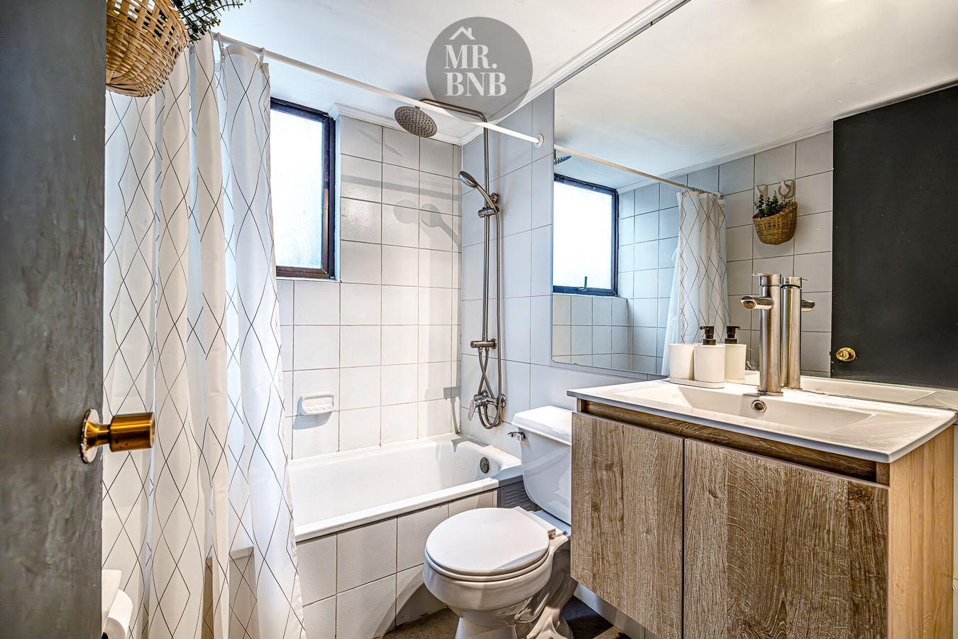 Baño con tina, cortina de baño, lavamanos con mueble de madera e inodoro