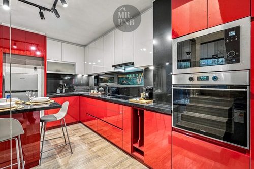 Cocina de muebles rojos con horno y microondas empotrados, campana y mesa alta con sillas