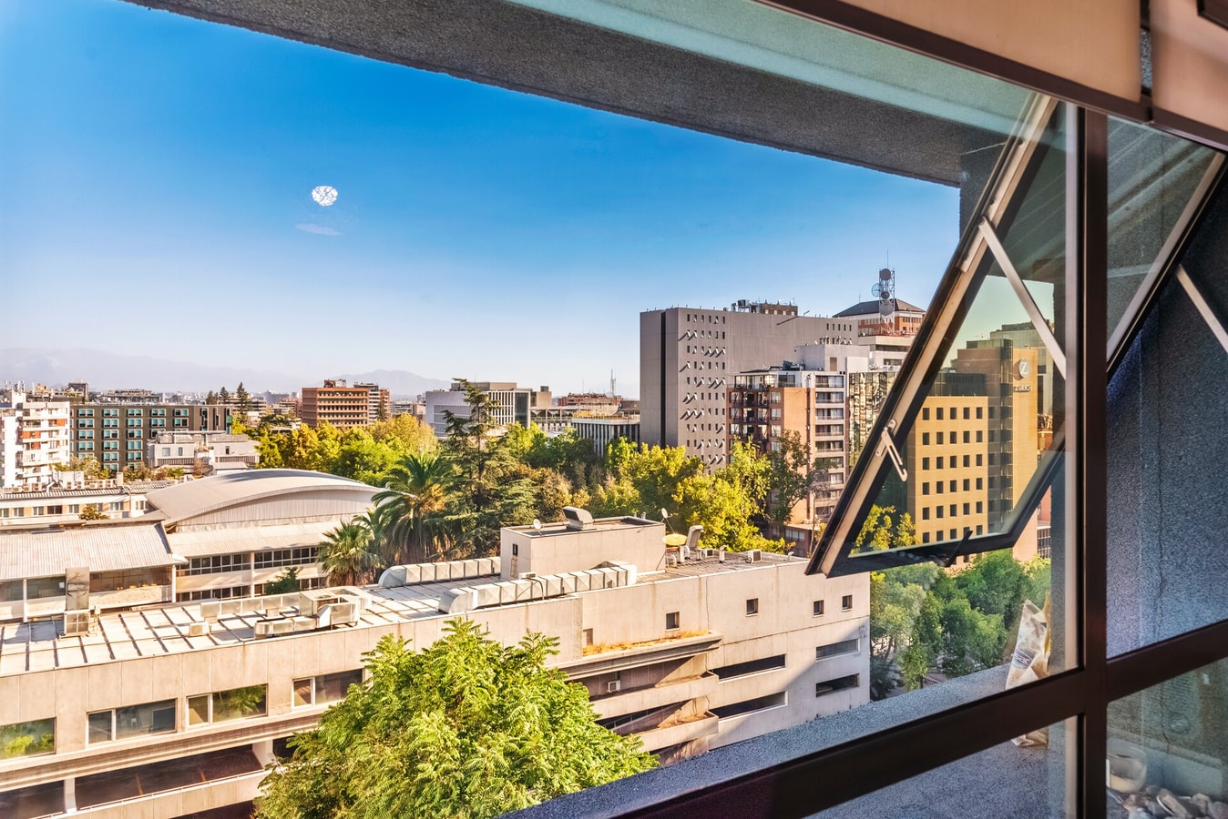 Vista desde ventana batiente hacia techos bajos y edificios de la ciudad