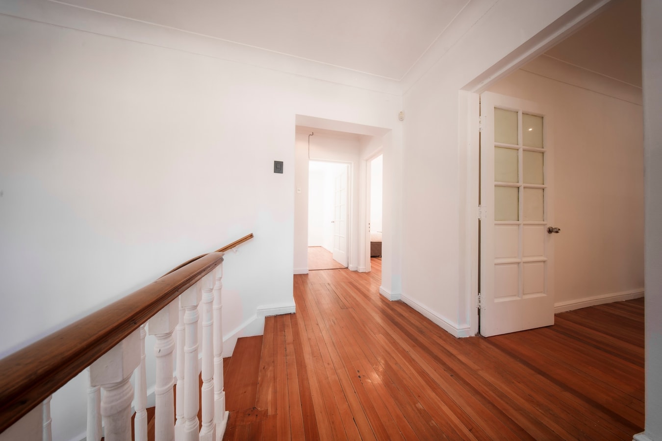 Pasillo del segundo piso sin amoblar, con piso de madera, baranda de balaustres blancos y puerta de vidrio repartido