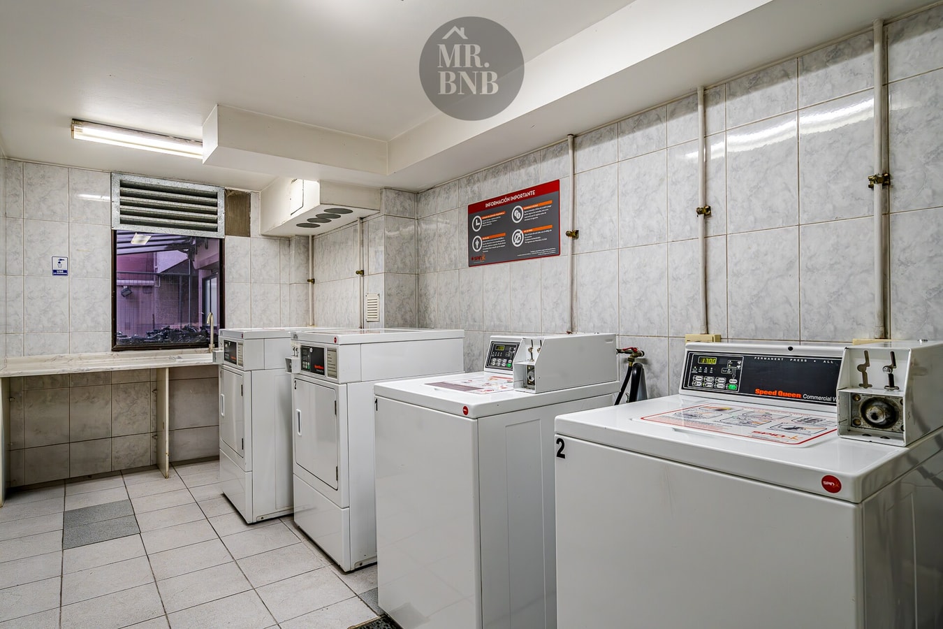 Sala de lavandería del edificio con varias lavadoras y secadoras industriales
