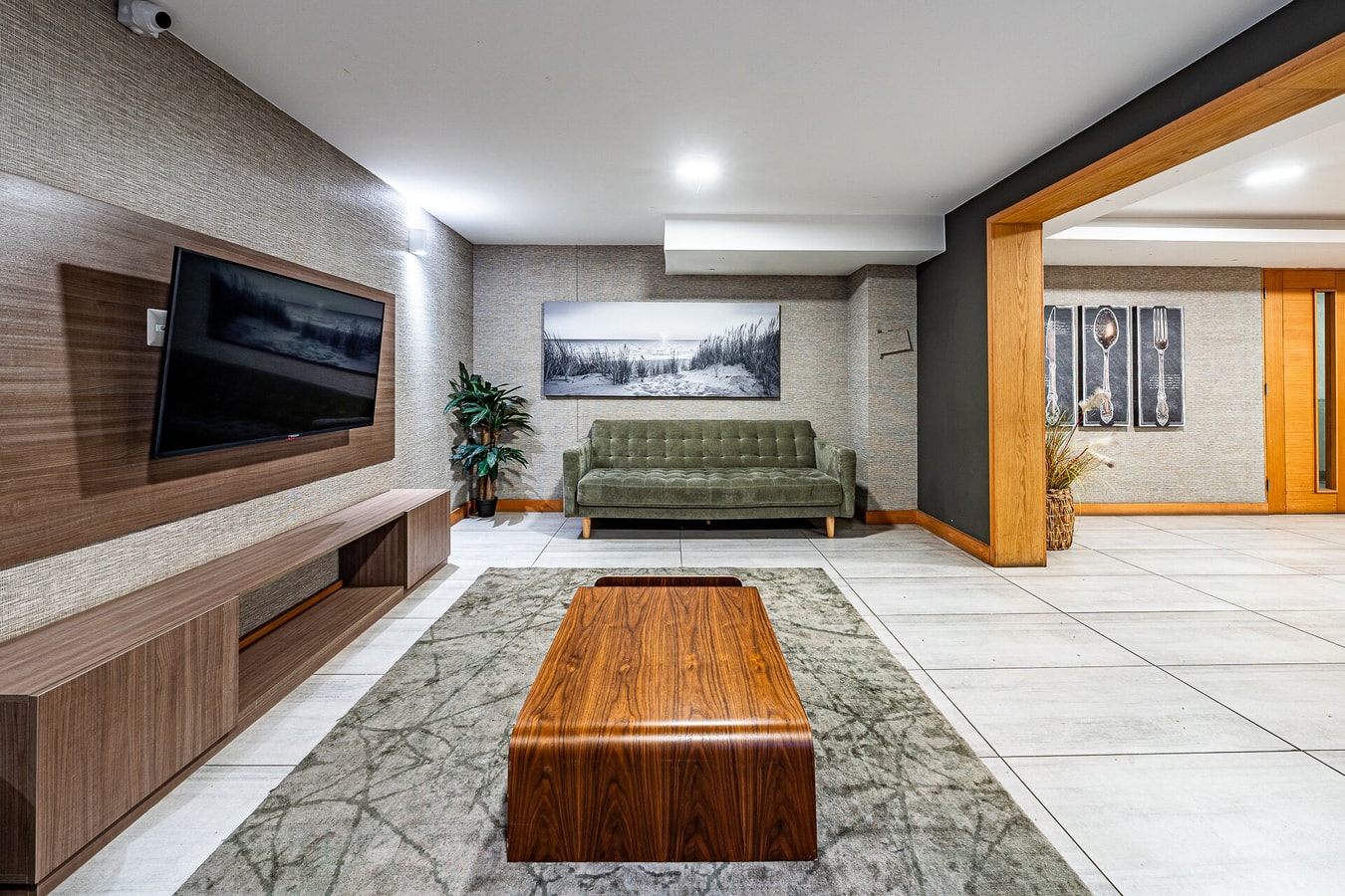 Salón común del edificio con televisor sobre mueble de madera, sofá verde, mesa de centro y alfombra
