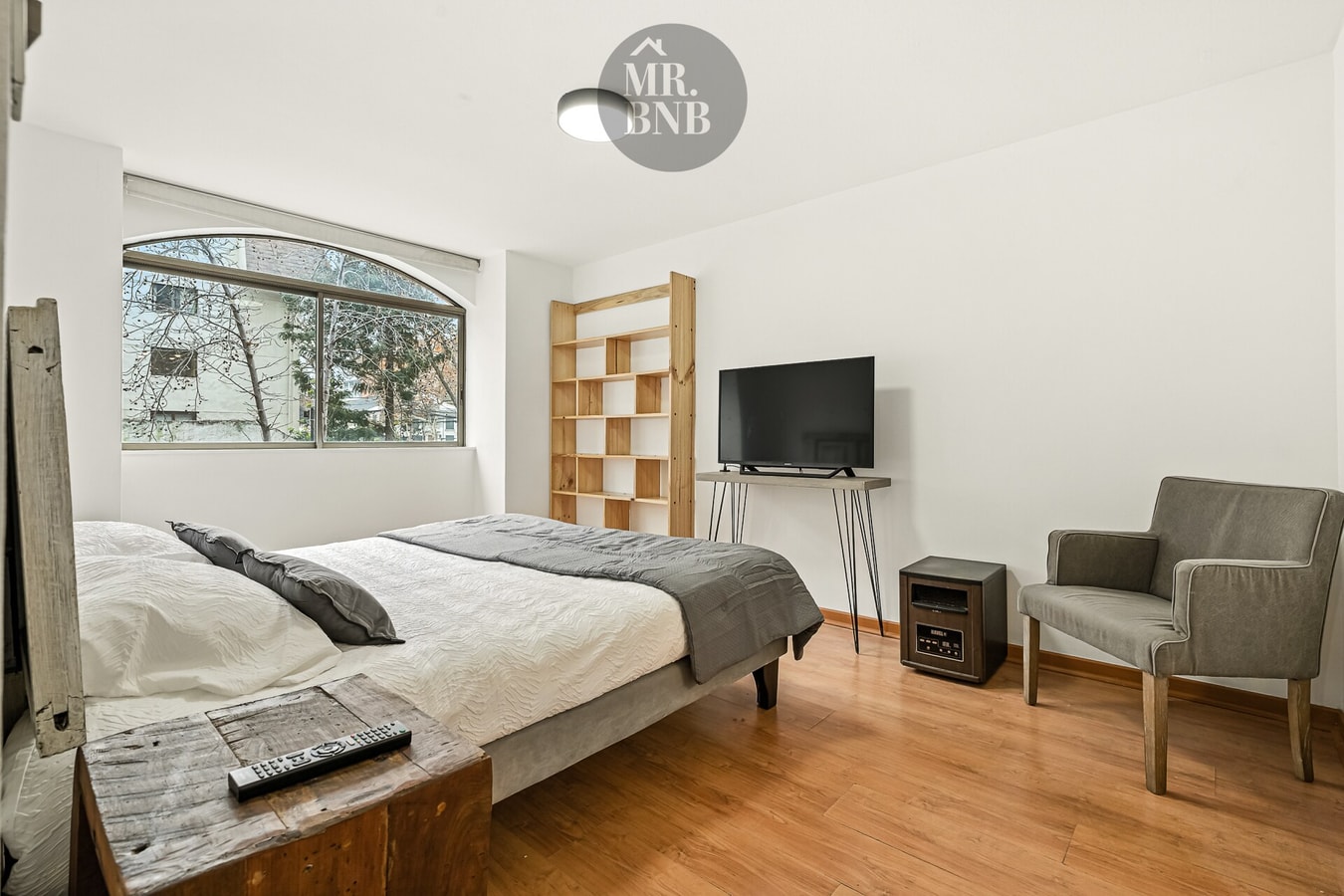 Dormitorio con cama matrimonial, TV, sillón y estructura de madera al fondo