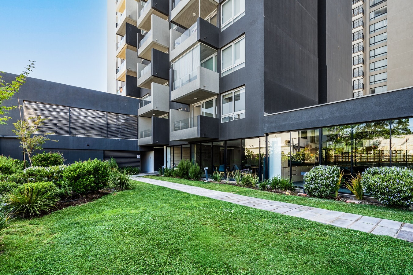 Áreas verdes del edificio con sendero pavimentado, césped y jardines.