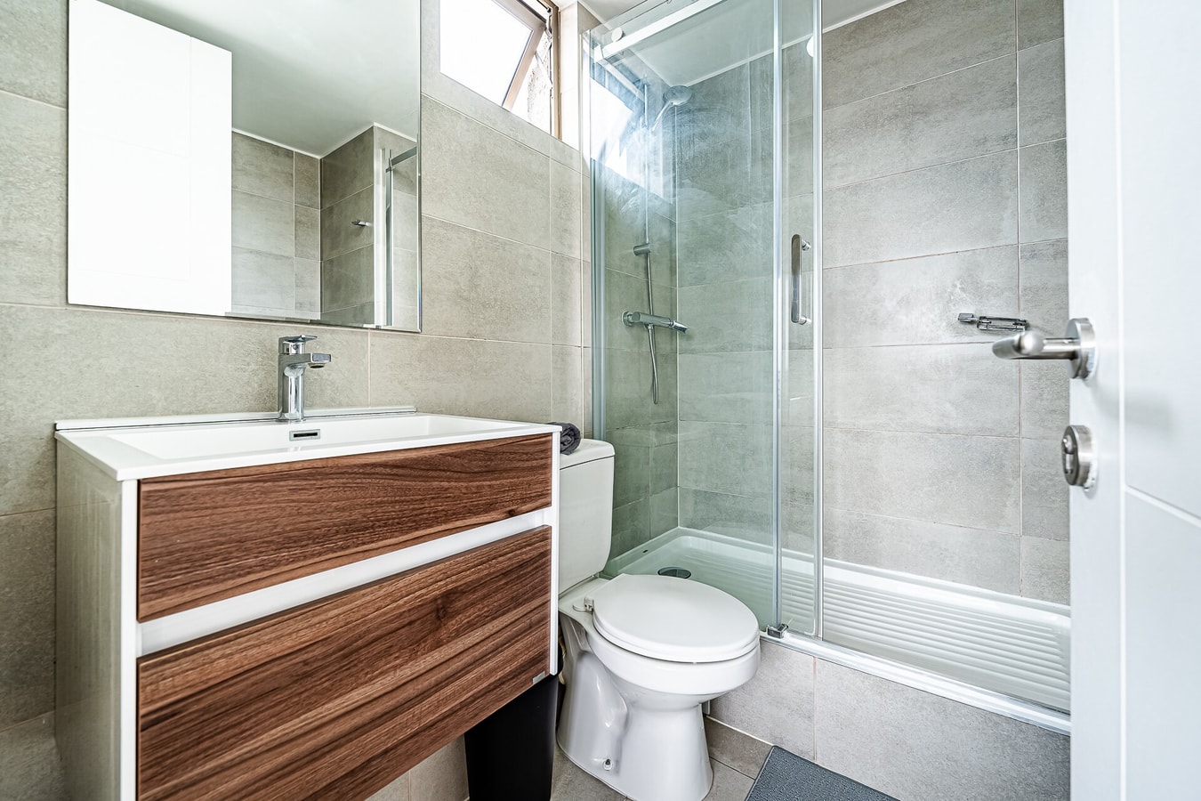Baño con ducha de vidrio, mueble vanitorio de madera y WC