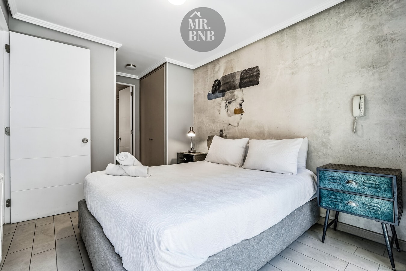 Dormitorio con cama, veladores de colores y teléfono en la pared
