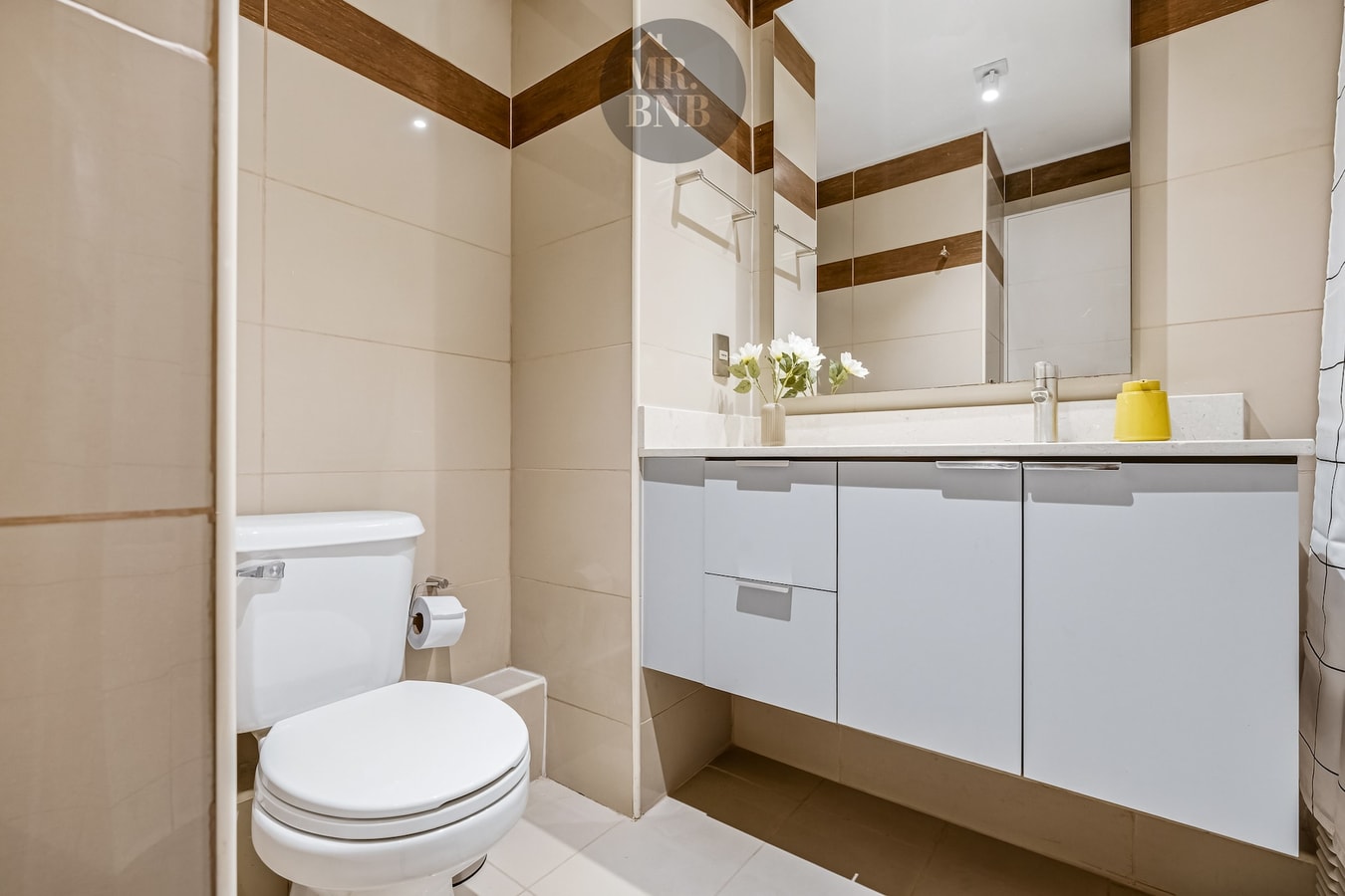 Baño con mueble vanitorio, espejo, flores sobre la encimera e inodoro