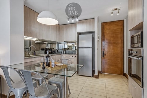 Cocina equipada con mesa de comedor, muebles de madera, horno, microondas y refrigerador.