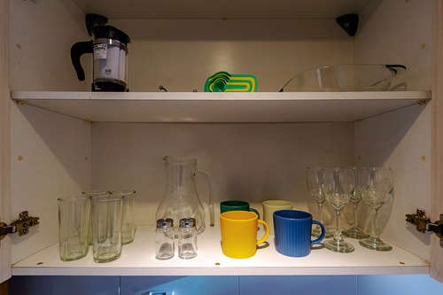 Repisa de cocina con vasos, tazas y utensilios de vidrio.