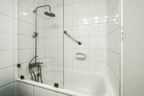 Detalle de ducha con tina, llave de agua caliente y repisa