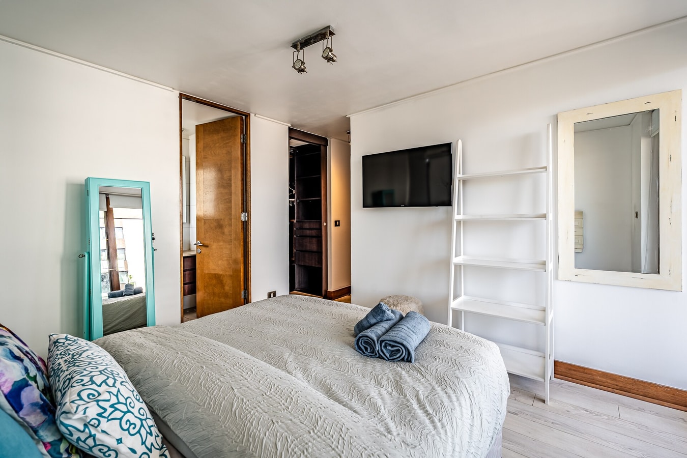 Dormitorio con cama, espejo de pie turquesa y repisas blancas
